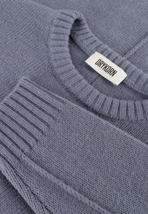 Gray knit sweater featuring a ribbed crew neckline and sleeve cuffs, with a textured pattern and a labeled tag. Soft, wool-like material.