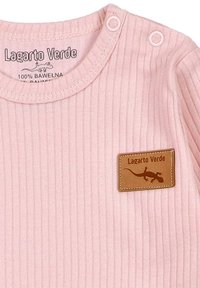 Rosa gerippter Baby-Overall mit Druckknopfverschlüssen und einem braunen Lederpatch, das eine Eidechse und den Text "Lagarto Verde" zeigt.