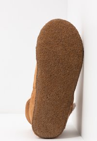 Wildlederstiefel mit einer strukturierten, braunen Gummisohle, die eine abgerundete Form und ein weiches, leichtes Innenfutter aufweist. Minimale Nahtdetails sind sichtbar.