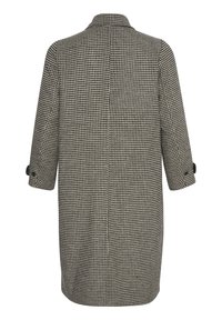Kappa i houndstooth-mönster i svart och vitt, med krage och trekvartslånga ärmar. Har knäppte manschettdetaljer och rak passform.