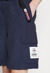 Námořnické cargo šortky s tkanou nášivkou s motivem globu a textem "TOMMY JEANS". Obsahují boční kapsy a černý pás.