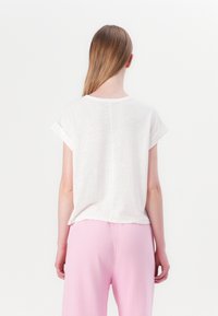 Hvid tekstureret kortermet T-shirt med oprejste manchetter, der har en central sømdetalje, båret med pink bukser.