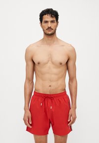 Rote Badeshorts mit einem Kordelzugbund, seitlichen Streifen und einem leichten Material. Das Design ist einfach und funktional.