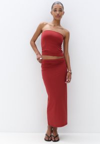 Rød to-delt sæt med en strapless top og en lang, tætsiddende nederdel lavet af glat stof. Designet inkluderer samlet detaljer ved taljen.