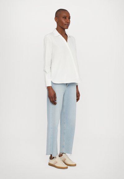 Vit långärmad skjorta med krage, tillsammans med ljusblå högmidjade jeans och beige sneakers med randiga detaljer.