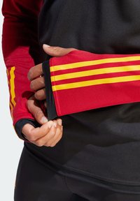 Camisa deportiva negra de manga larga con acentos a rayas rojas y amarillas en las mangas. Presenta un ajuste ceñido y flexible, y una textura suave.