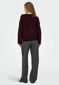 Burgunderfarbener Strickpullover mit oversized Passform, lässig fallenden Schultern und langen Ärmeln, kombiniert mit hochtaillierten grauen, maßgeschneiderten Hosen.
