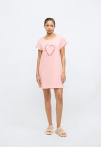 Ροζ βαμβακερό νυχτικό με κοντά μανίκια, με σχέδιο καρδιάς από κείμενο. Φοράει με μπεζ χνουδωτές παντόφλες. Απλή, άνετη εφαρμογή.