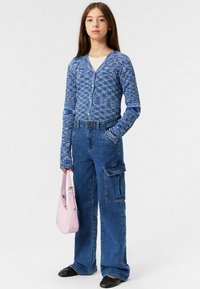 Blå mönstrad cardigan, högmidjade denimcargobyxor, rosa handväska, svarta skor. Byxorna har sidofickor som detalj.