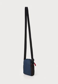 Borsa a tracolla blu navy e nera con texture liscia, tracolla regolabile e pull della cerniera rosso. Forma quadrata con scomparto principale con zip.