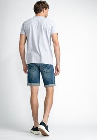 T-shirt gris à manches courtes associé à un short en denim retroussé. Le short est bleu foncé avec une texture délavée et des poches arrière. Chaussures décontractées.