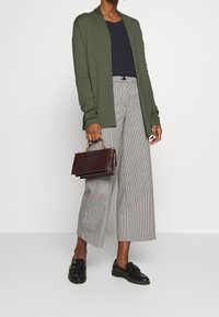 Olivgrön lätt cardigan, marinblå topp, grå och röd rutmönstrad culotte, svarta loafers, håller en bordeauxfärgad håndväska med krokodilmönster.
