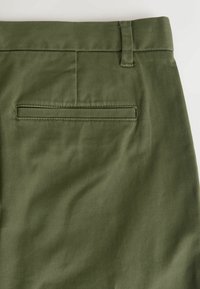 Olijfgroene broek van gladde stof met een platte voorkant, taillebandlussen en een enkele achterzak met een horizontale klepdetail.