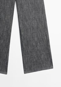 Partie inférieure d'un pantalon droit en tissu denim gris foncé avec coutures visibles sur fond blanc.