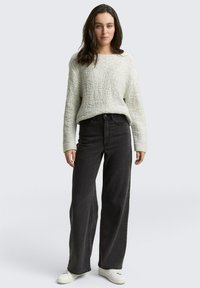 Pull léger gris texturé avec des manches longues, associé à un jean noir à taille haute et large, et des baskets blanches. Tenue simple et décontractée.