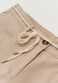 Beige Stoffshorts mit einem elastischen Bund und einem geflochtenen Kordelzug. Mit metallischen Enden am Kordelzug und genähten Taschen.