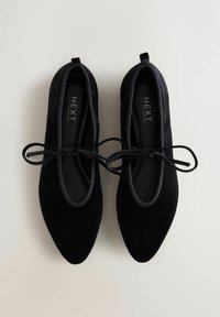 Balerini negre din suede cu vârful ascuțit și accente de fundiță ajustabile. Prezintă o suprafață texturată și o branț moale pentru confort.