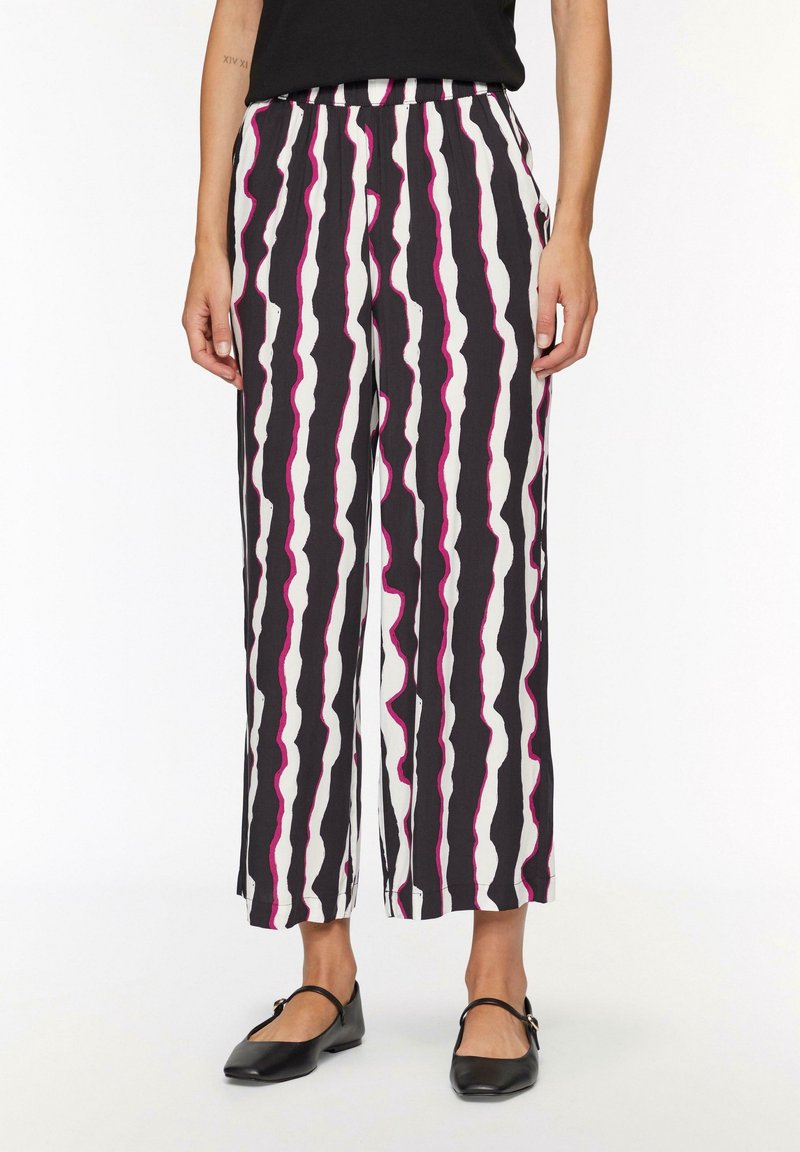 Pantalons noir et blanc à jambe large avec des rayures roses ondulées, dotés d'une taille élastique et d'un tissu léger. Associés à des ballerines noires.