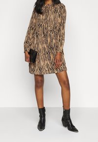 Keltainen mekko mustilla pystyviivoilla, pitkät hihat ja napituksen etuosa. Yhdistetty mustiin krokotiilihermoitukseen polvisukkiin ja laukun kanssa.