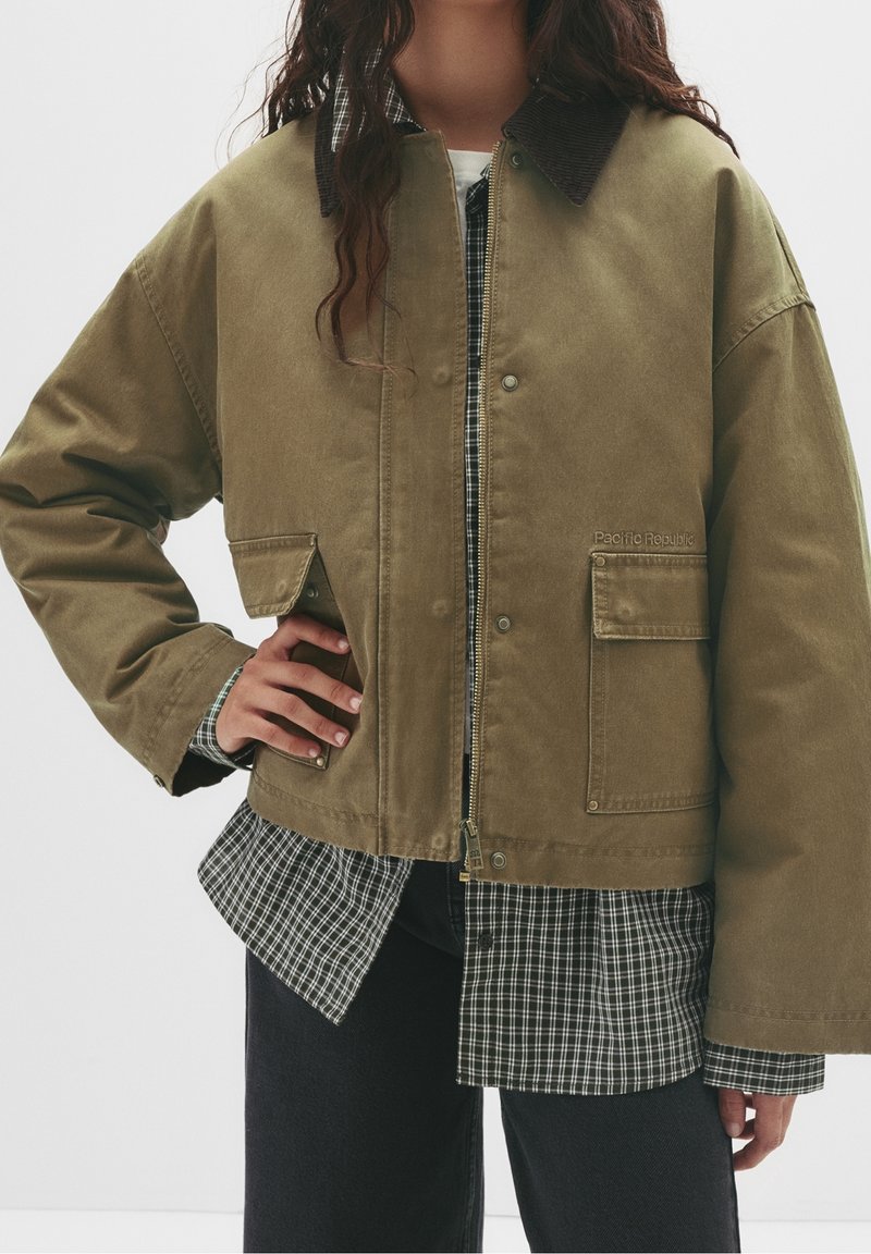 Veste courte vert olive en toile avec col en velours côtelé, dotée d'une fermeture éclair, de poches avant et d'un détail de logo brodé.