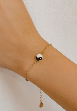 Gold chain bracelet featuring a round yin-yang charm, alternating black and white. Adjustable length with a small heart-shaped accent.
