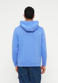 Svetlo modrá mikina s kapucňou na šnúrku, rebrovanými manžetami a lemom. Vyrobená z mäkkej tkaniny, s hladkou štruktúrou a voľným strihom.