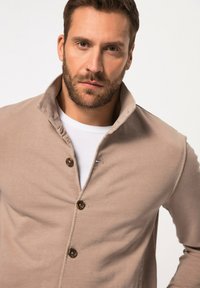 Beige blazer med krave og knaplukning, lavet af blødt stof. Har en struktureret overflade og et minimalistisk design.