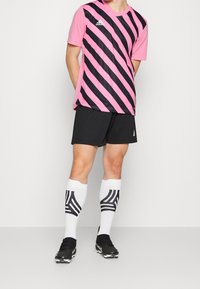 Maglia sportiva a righe rosa e nere, pantaloncini neri, calzini bianchi con motivo nero e scarpe da calcio nere. Leggera, vestibilità atletica.