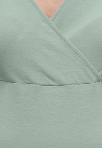 Κοντινή λήψη απαλού ανοιχτοπράσινου υφάσματος με V-λαιμόκοψη και ραφές στην περιοχή του πάνω μέρους του στήθους.