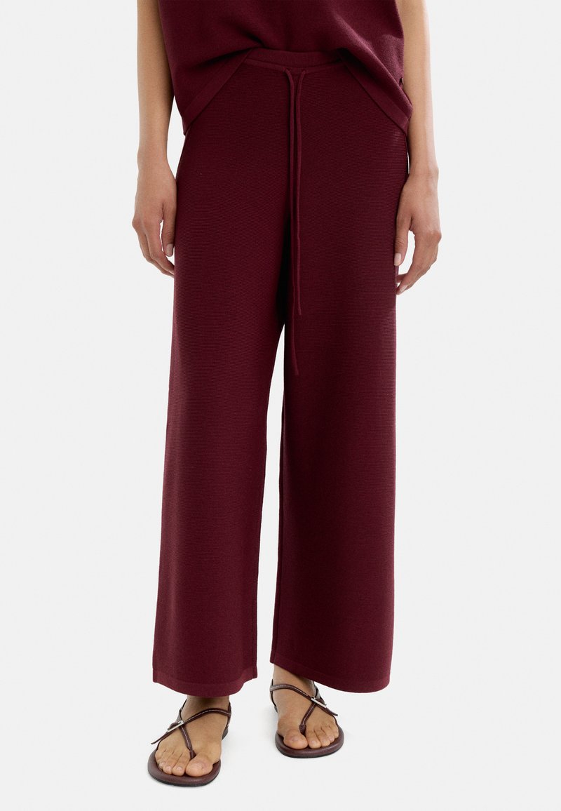 Burgundowe spodnie wide-leg z teksturowanym wykończeniem, z elastycznym pasem i sznurkiem do regulacji. Połączone z prostymi brązowymi sandałami.