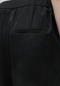 Κοντινό πλάνο μαύρου παντελονιού με ελαστική μέση και μία οριζόντια πίσω τσέπη στη δεξιά πλευρά.