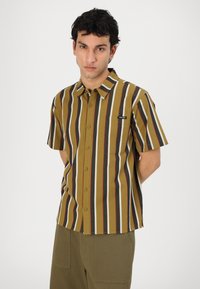 Short-sleeve shirt featuring horizontal stripes in olive, black, white, and red. Made of smooth fabric with a buttoned front and chest pocket.