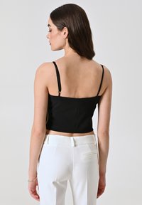Zwart cropped top met dunne bandjes, gladde textuur en een aansluitend ontwerp. Gecombineerd met witte, op maat gemaakte broeken met een achterzak.