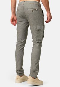 Pantalones cargo en gris, ajustados, con bolsillos en los laterales y en la parte trasera, y detalles de costura. Se llevan con zapatillas de color claro.