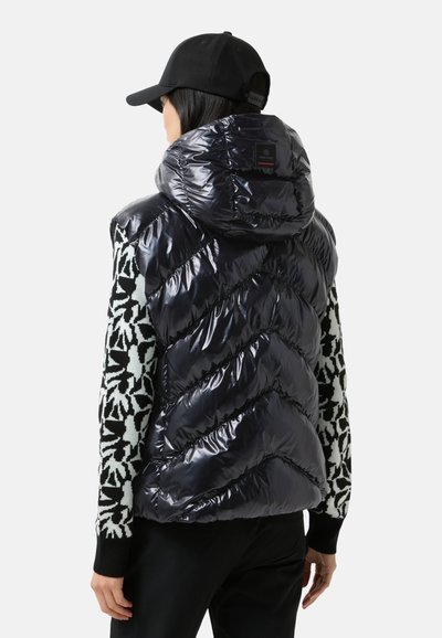 Błyszcząca granatowa kamizelka puchowa z wysokim kołnierzem, wzorem w zygzak oraz czarno-białymi rękawami. Regulowany kaptur i zamek błyskawiczny.