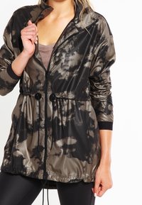 Vattenavvisande jacka i svart och taupe batikmönster. Har dragkedja framtill, elastisk midja och två framknappar.