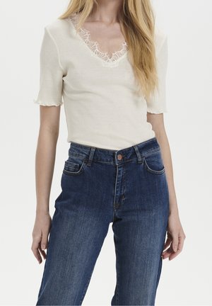 Top blanco acanalado con borde de encaje en el escote y mangas cortas con borde ondulado, combinado con jeans de mezclilla azul oscuro de cintura alta.