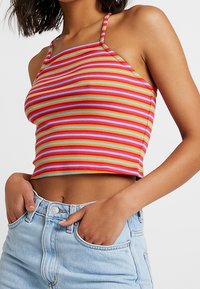 Top corto a rayas con finas tirantes en rojo, naranja, amarillo y azul; textura acanalada; combinado con pantalones cortos de mezclilla claros de tiro alto.