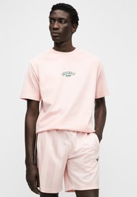 Ροζ βαμβακερό t-shirt με το λογότυπο "ORIGINALS" σε πράσινο, συνδυασμένο με ροζ σορτς με διακριτικές κάθετες ρίγες και πλαϊνές τσέπες.