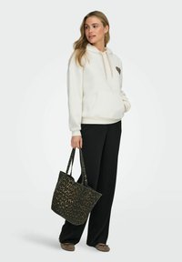 Kremfarget hettegenser med hjerte i leopardmønster, kombinert med svarte vide bukser. En leopardmønstret totebag og brune flate sko fullfører antrekket.