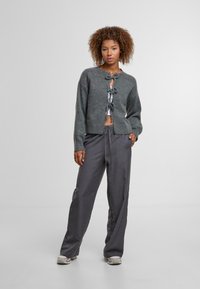 Grauer, kürzer geschnittener Cardigan mit Bindebändern vorne, kombiniert mit grauen, weit geschnittenen Hosen. Glatte Textur und lässiges Design.