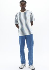 Striped cotton t-shirt in white and blue, round neckline, paired with light blue jeans and gray athletic shoes featuring reflective accents.