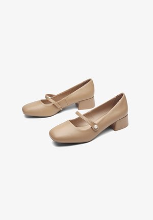 Des chaussures Mary Jane en cuir nude avec un bout arrondi, un petit talon carré et un petit accent en perle sur la sangle. Texture lisse, design simple.