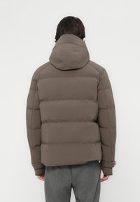 Brun pufferjakke med hætte, med en quiltet design, elastiske manchetter og en glat tekstur, set fra ryggen.
