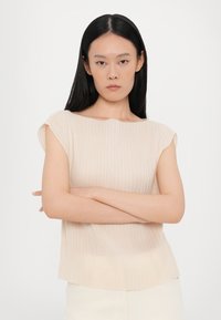 Light beige ribbed top with a wide boat neckline and cap sleeves, featuring a soft texture and a gently curved hemline.