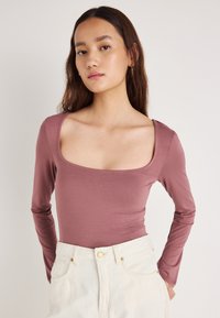 Pika varrukaga vormitud pluus pehmes lavendli toonis kangas, ruudukujulise kaelusega. Ülikõrge vöökohaga valgete teksadega, millel on kuldsed detailid.