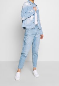 Světlá modrá džínová bunda s opranými detaily, kombinovaná se světlými modrými džínami a bílými teniskami. Hladká textura, pohodlný střih a klasický design.