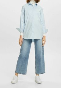 Ljusblå skjorta med knappar och långa ärmar, i kombination med vida ljusblå denimjeans och vita sneakers. Slät tygkvalitet, avslappnad design.