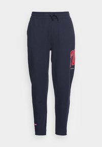 Tmavě modré tepláky s elastickým pasem a stahovací šňůrkou. Na levé noze je červený nápis "TO NY". Měkká, hladká textura látky.