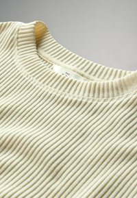 Krämfärgad ribbad stickad topp med en rundad crewneck och mjuk textur, med synliga stygn vid kragen och nederkanten.